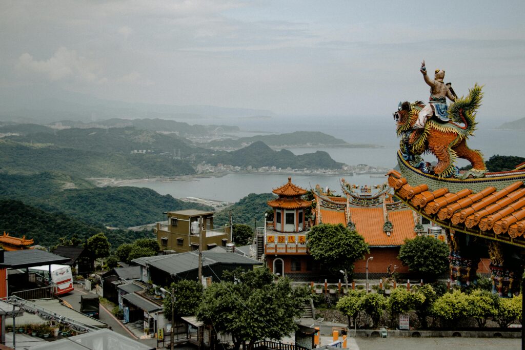 Explore the breathtaking view of a traditional Asian temple with intricate architecture amidst lush greenery and mountainous backdrop.