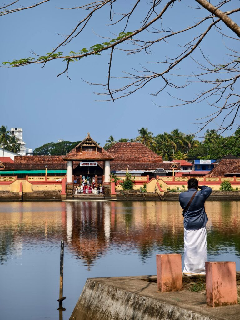 A man photographs a temple scene by a reflective pond during the day.